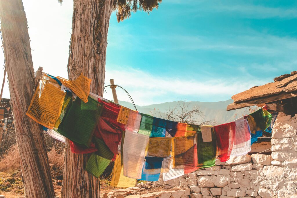 Vibrant prayer flags hanging in Bhutan, against a scenic mountain backdrop under a clear blue sky.